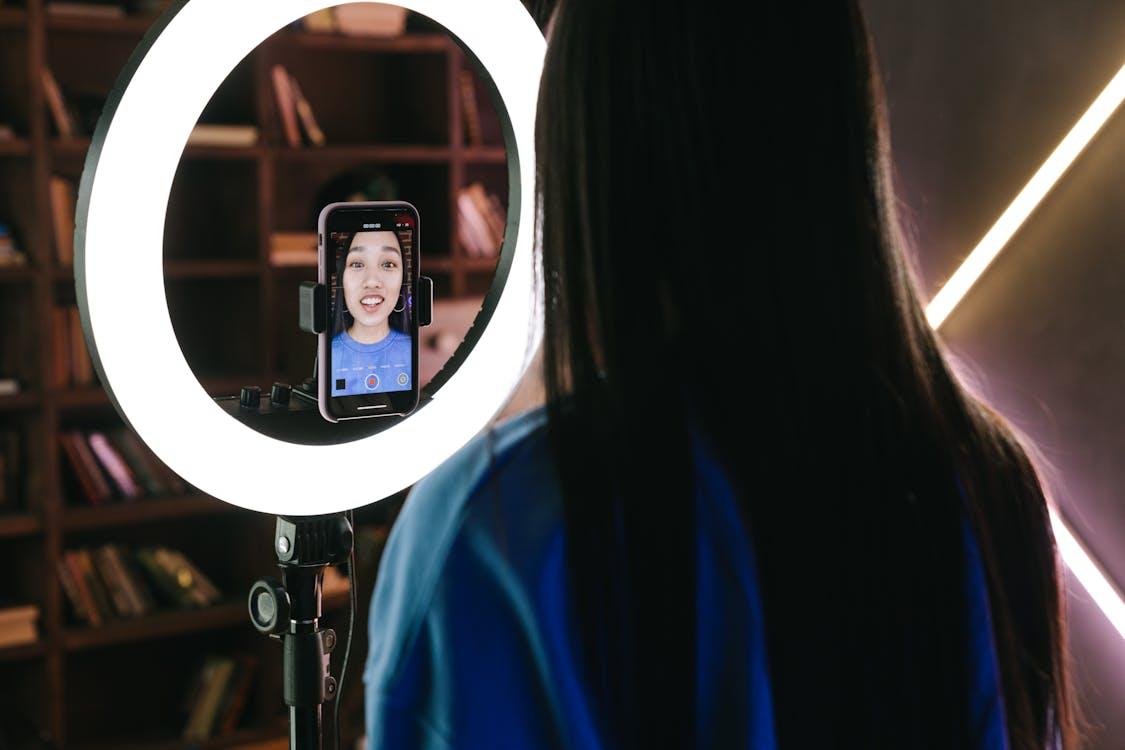 A person recording themselves with a smartphone attached to a ringlight