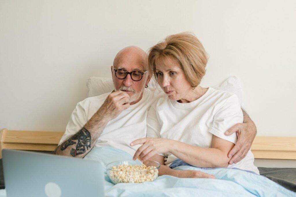 Two people eating popcorn while watching a movie on a laptop