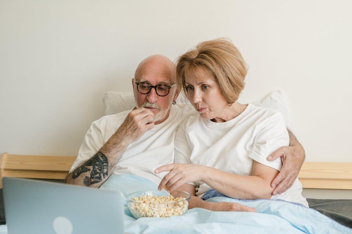 Two people eating popcorn while watching a movie on a laptop
